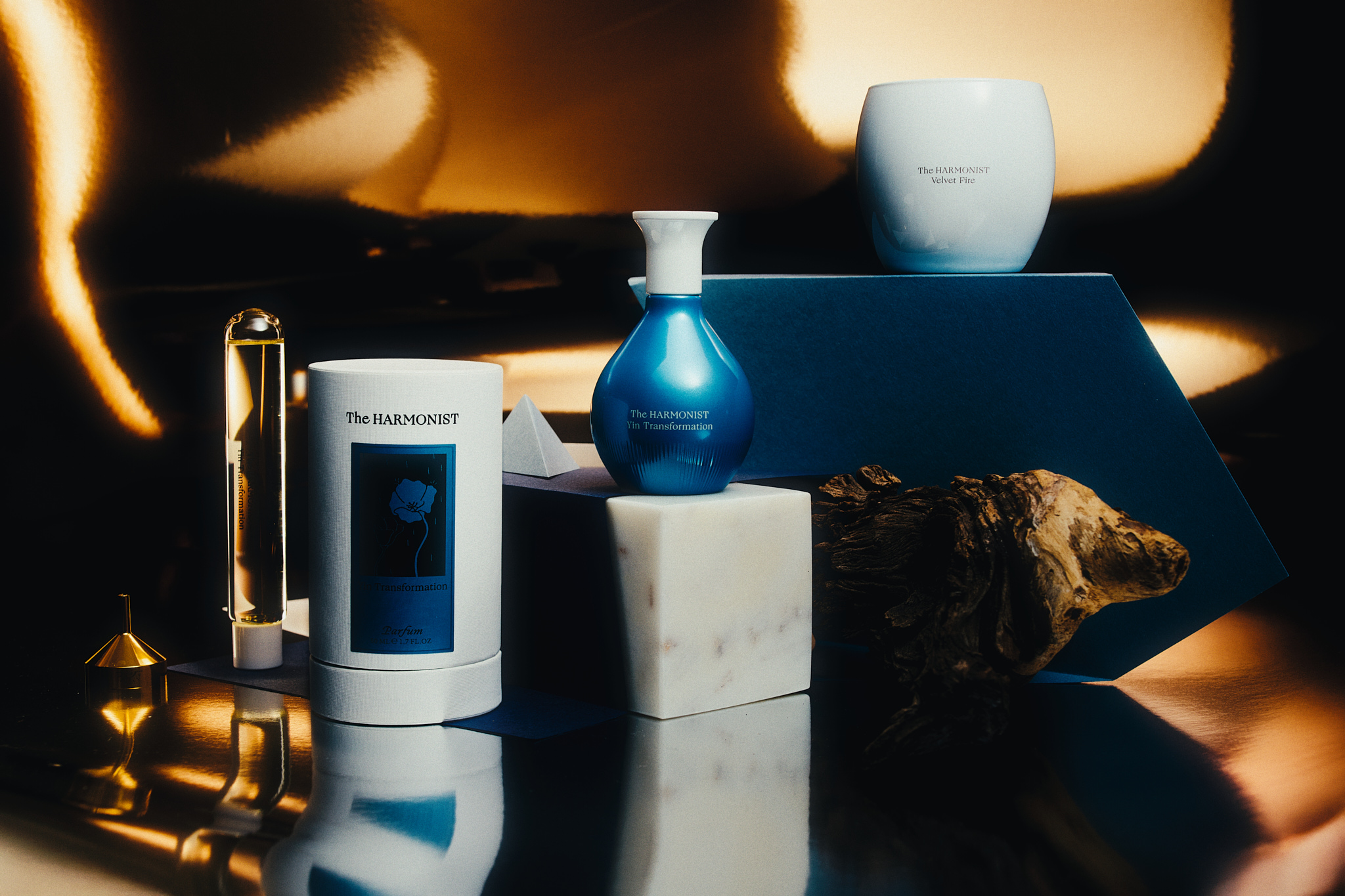 Still life of The Harmonist fragrance bottles, containers on marble and blue stands with driftwood.