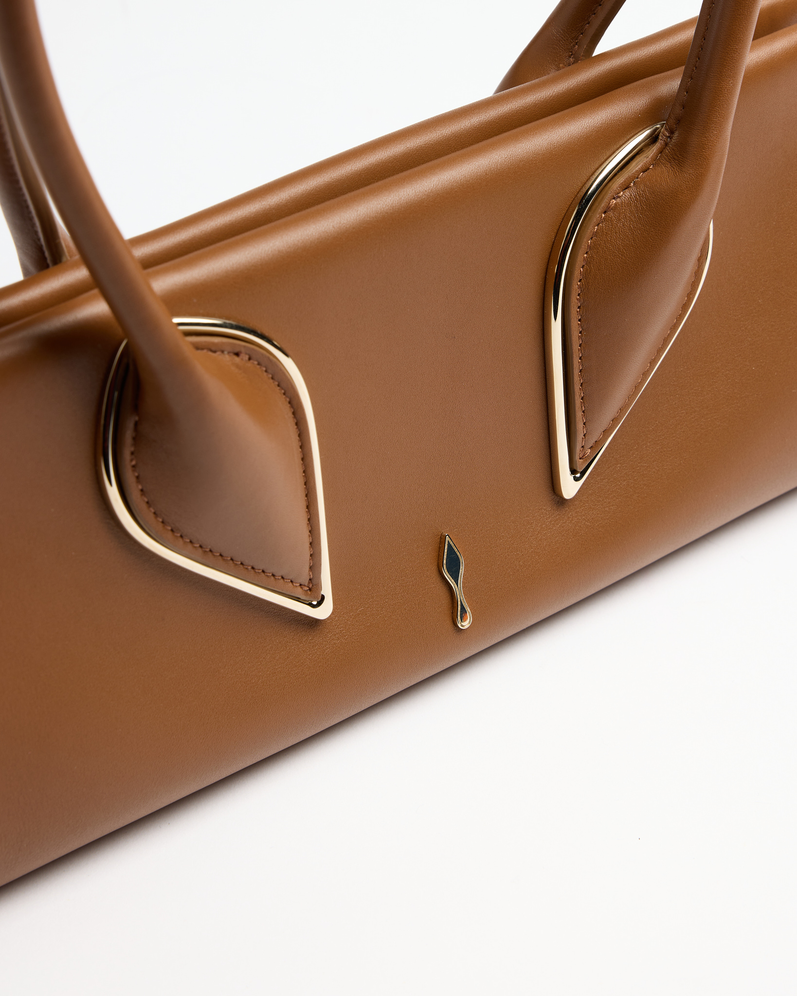 Brown leather handbag with two handles, gold metal accents, and a small emblem on front.